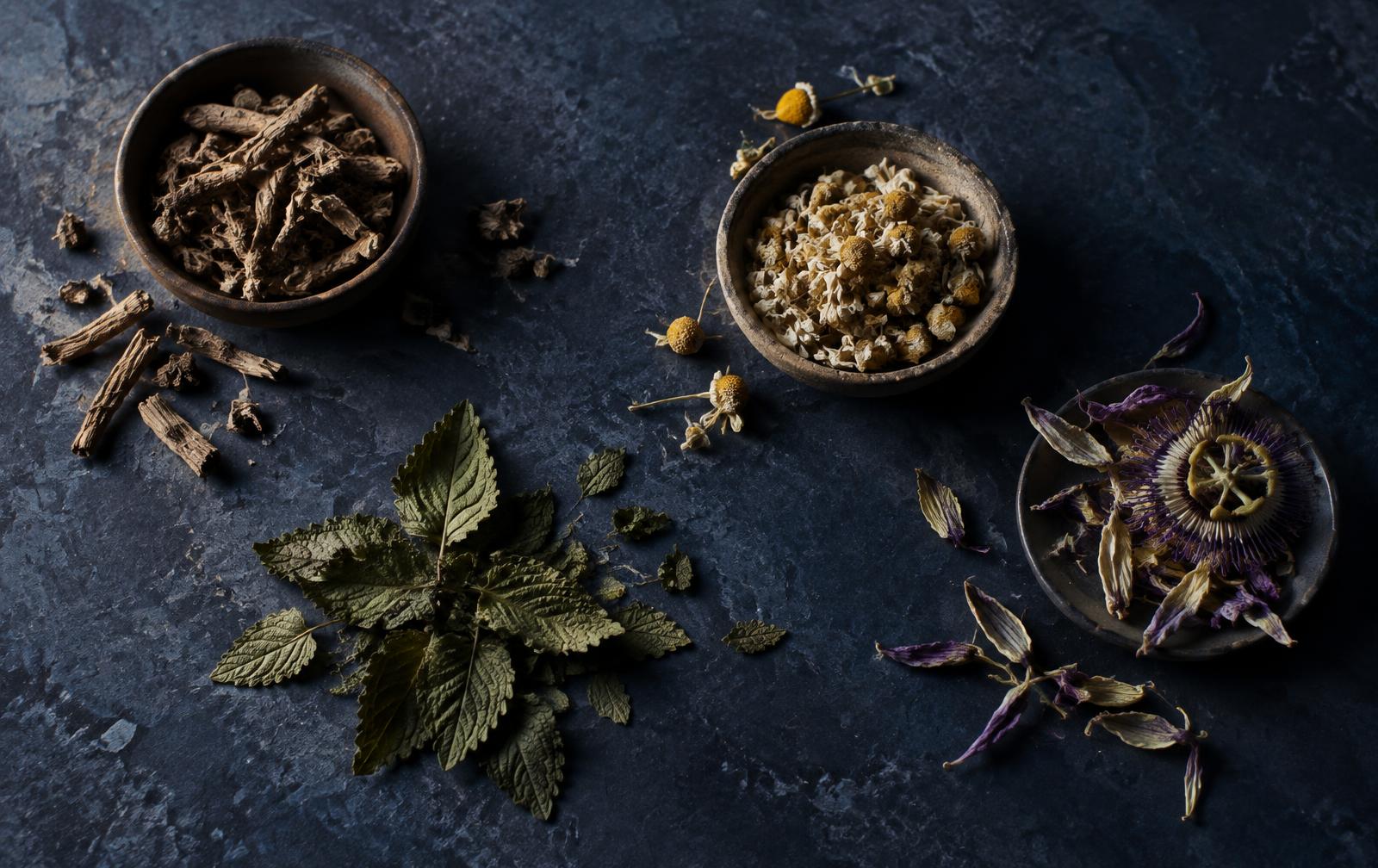 Dried valerian root, chamomile flowers, lemon balm leaves and passion flower on dark stone
